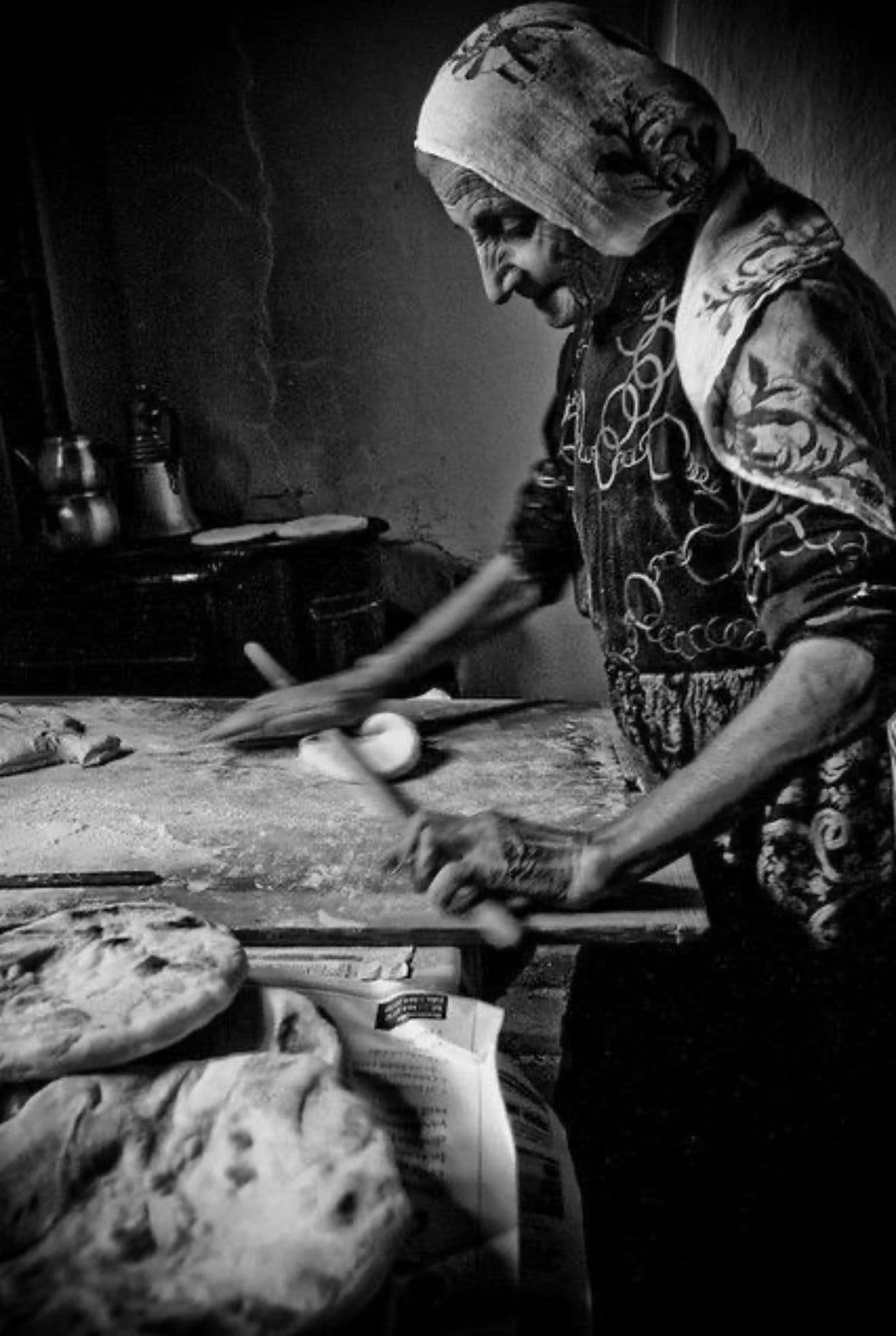 Historische Schwarz-Weiß-Aufnahme einer älteren Frau beim Brotbacken